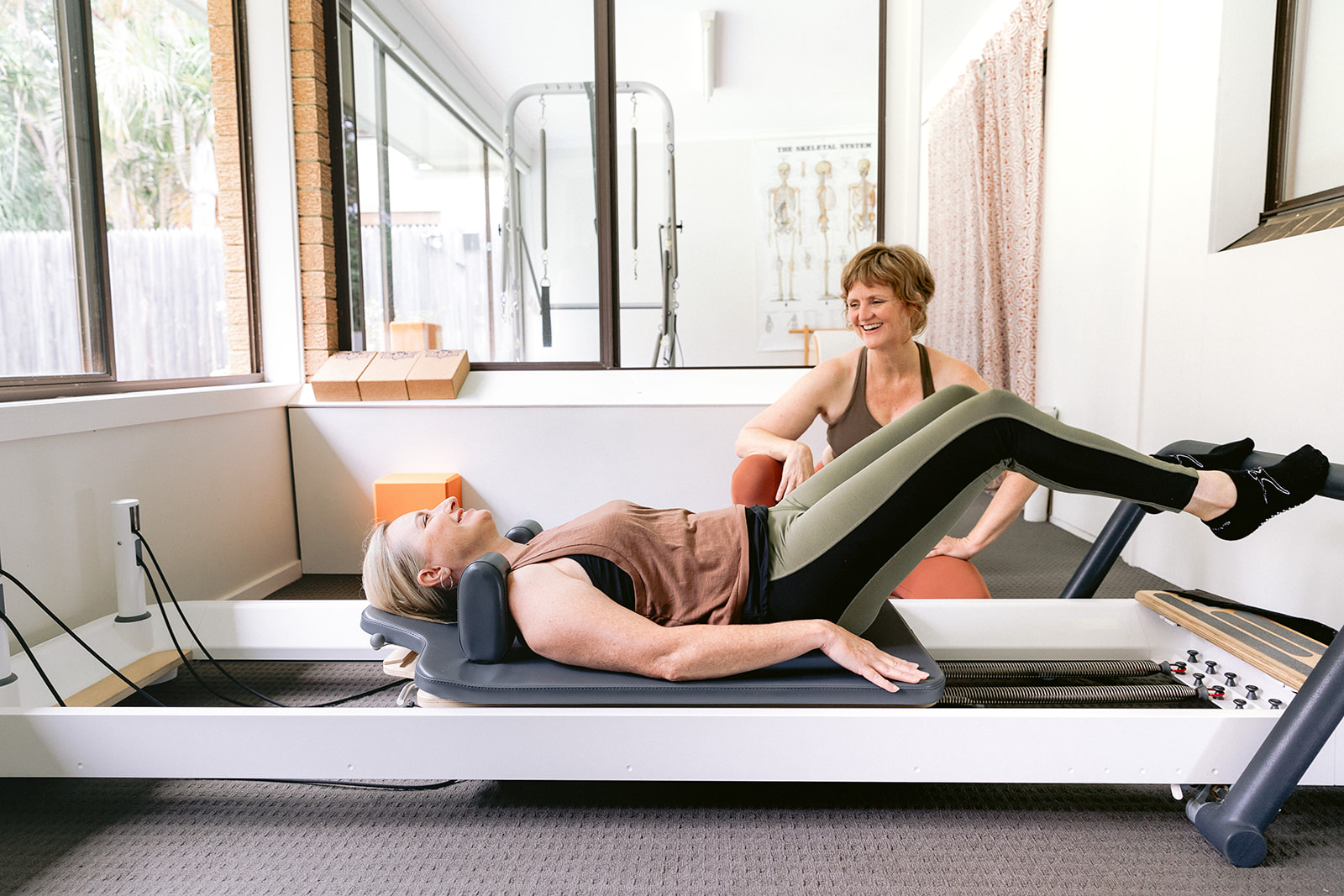 Woman on a reformer smiling at her teacher.