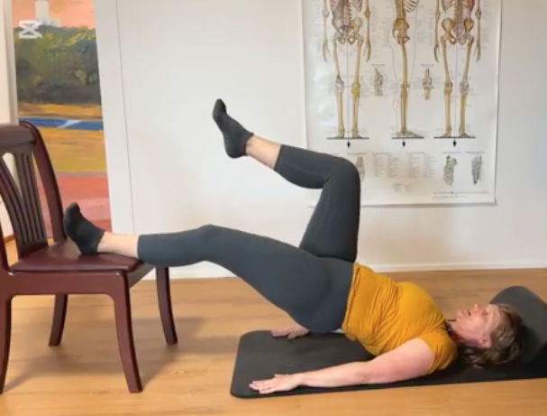 Woman lying prone with feet on a chair working her hamstrings.